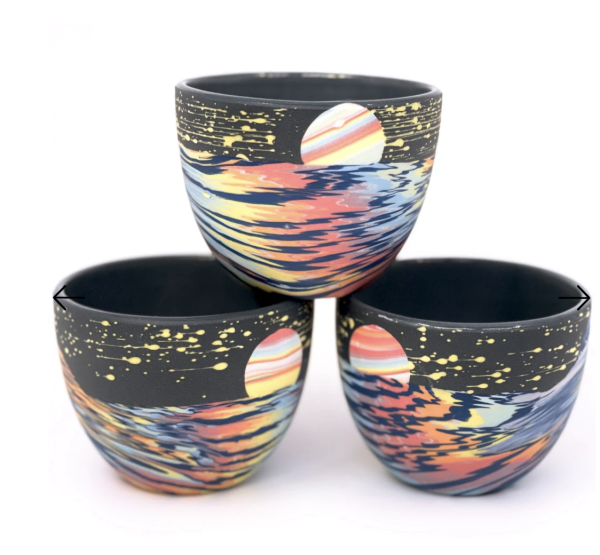 Three bowls stacked in a pyramid. The design of each bowl is a black base with bright colors splashed across, and a moon shape rising above.